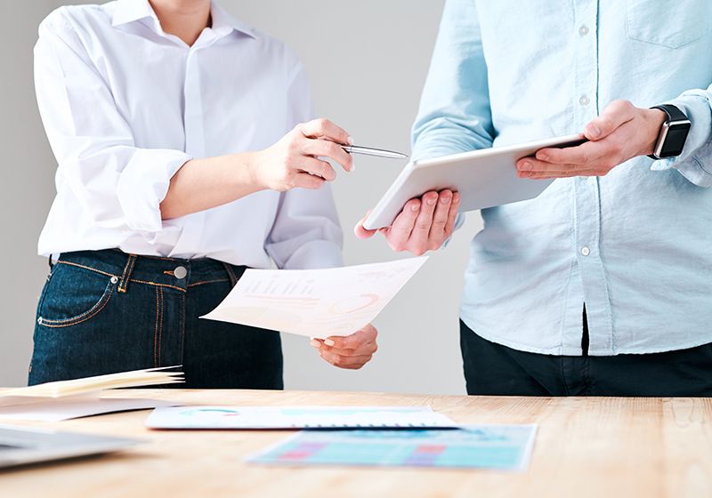 Close-up of unrecognizable man holding tablet while discussing marketing plan with colleague in office